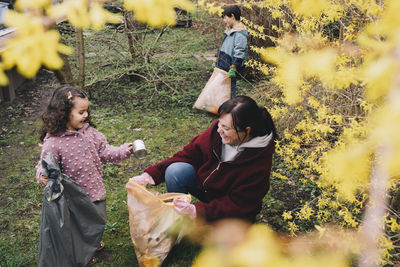 Happy daughter helping mother in collecting waste at backyard