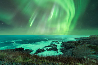 Scenic landscape of rocky coast washed by endless north sea under colorful polar lights at night on lofoten island