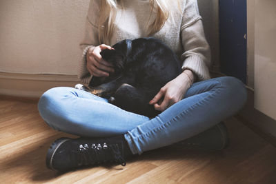 Low section of woman with dog sitting on floor at home