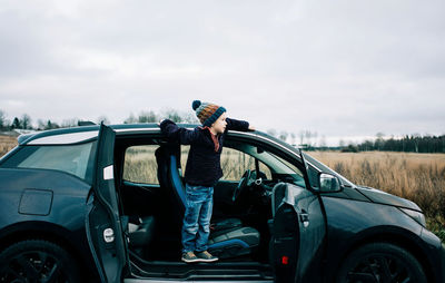 Man standing on car against sky