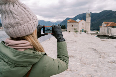 Rear view of woman photographing through camera against sky