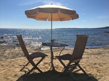 Chairs and table on beach against sky