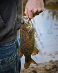 Midsection of man holding fish at lake