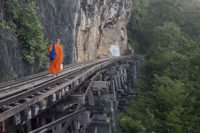 Rear view of monk walking on railroad tracks by mountains
