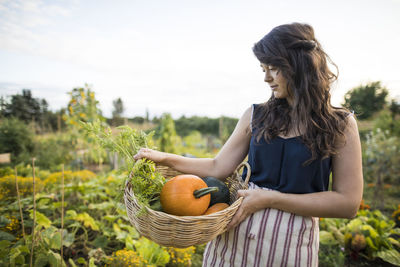 Woman looking at vegetables while carrying it in basket at community garden