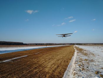 Airplane flying over landscape against blue sky