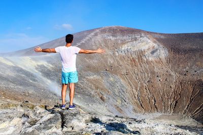 Rear view of man with arms outstretched standing at volcano
