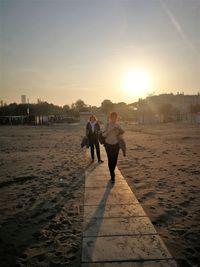 Women standing on footpath at beach during sunset