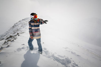 Full length shot of a cheerful skier carrying her skis on her shoulder. a skier is standing on top