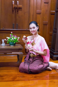 Smiling beautiful woman wearing traditional clothing and jewelries while holding floral garland at home