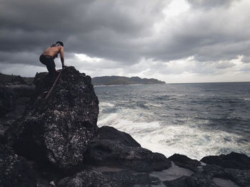 Man standing on rock by sea against sky