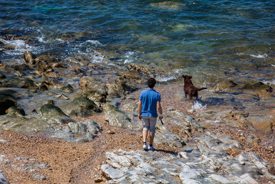 Rear view of men standing on rock by sea