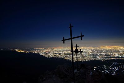 Silhouette cross on landscape against sky at night