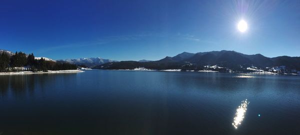 Scenic view of lake by mountains against blue sky on sunny day