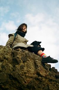 Low angle view of woman sitting on rock against sky