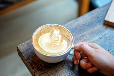 Cropped image of hand holding coffee cup on table