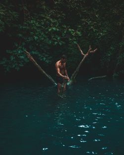 Shirtless man standing in river at forest