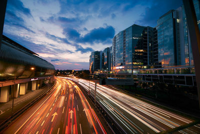 Light trails on road amidst buildings against sky at night