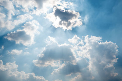 Low angle view of sunlight streaming through clouds