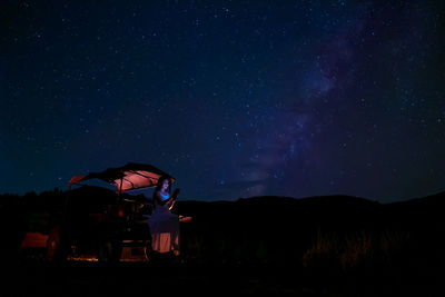 A woman sits in a farmer's automobile, gazing at the stars in the night sky, with the milky way .