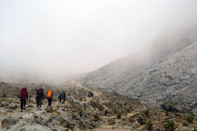 Rear view of people walking on mountain against sky