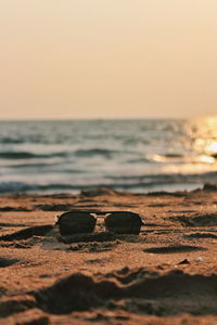 Close-up of sunglasses on beach against clear sky