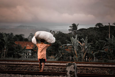 Rear view of man standing by railroad tracks against sky