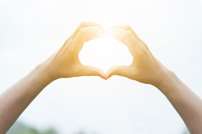 Cropped hands of woman making heart shape against bright sun