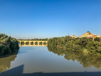 Reflection of building in lake against clear blue sky