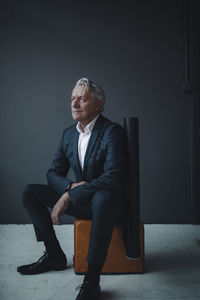 Senior businessman sitting on old-fashioned suitcase