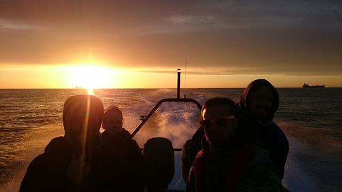 Friends enjoying in boat on sea against cloudy sky during sunset