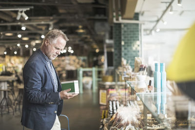 Side view of mature man reading label on food package in supermarket