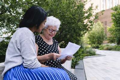 Surprised senior woman reading letter sitting by daughter at park