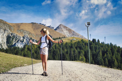 Full length of hiking woman standing by tree against sky and mountain 