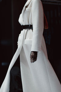 Fashion details of long insulated autumn winter white coat with black belt. fashion model walking