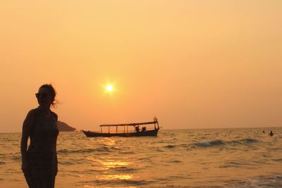 Woman standing by sea against sky during sunset
