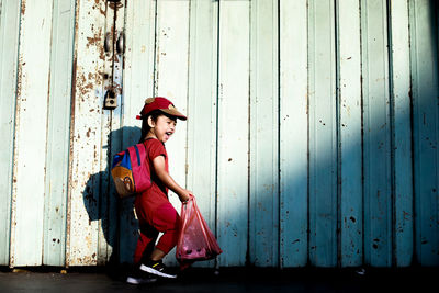 Side view of girl with backpack standing against wall