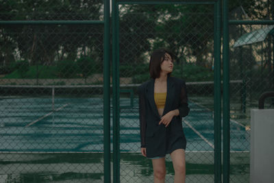 Full length of woman standing by chainlink fence