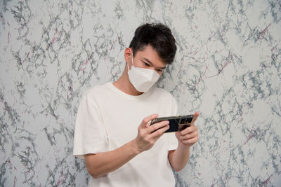 Young man using mobile phone against wall