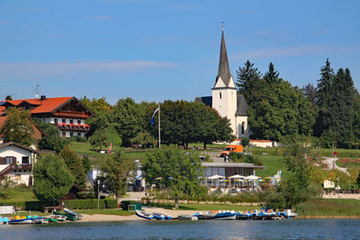 Sailboats by building and trees against sky