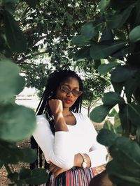 Portrait of beautiful young woman standing amidst trees on field