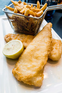 Close-up of fried fish with lemon by potato chips in tray on table
