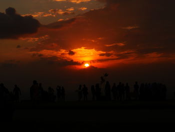 Silhouette people against orange sky during sunset