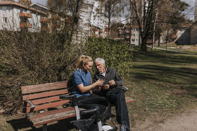 Female caregiver giving fruits to senior man sitting on bench at park