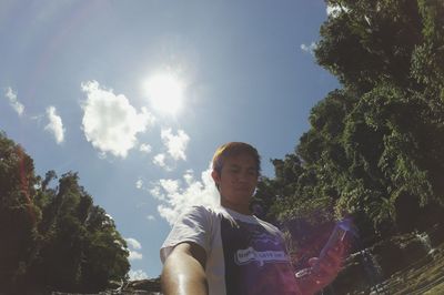 Low angle view of thoughtful young man using phone against sky at sunny day