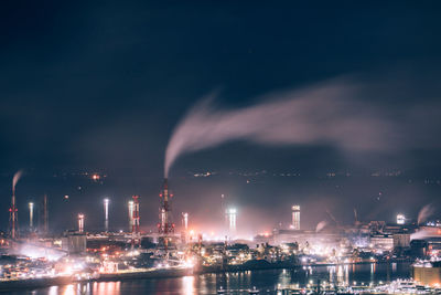 Illuminated factory against sky at night