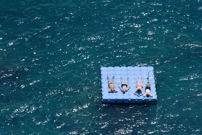 High angle view of shirtless friends relaxing on diving platform in sea