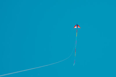 Low angle view of kites flying against clear blue sky