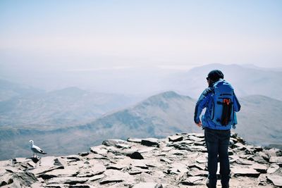 Rear view of hiker standing on mountain against sky