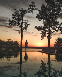 Silhouette person by lake against sky during sunset